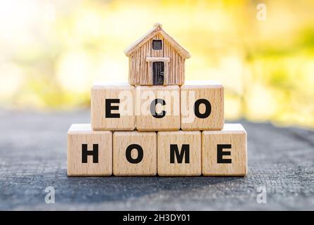 Petite maison de jouets debout sur des blocs de lettre en bois lisant ECO HOME sur un fond de forêt d'automne flou.Concept de maison à faible impact sur l'environnement. Banque D'Images