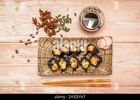 Assiette à sushis rouleau de riz uramaki japonais teint à l'encre de calmar, farci de saumon, de macago roe, d'avocat mûr, de sauce soja et de baguettes Banque D'Images