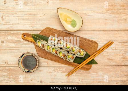 Vue de dessus de sushi en rouleau de californie uramaki avec graines de sésame, algues de nori, fromage à la crème, saumon et avocat mûr avec wasabi, sauce soja et bois Banque D'Images