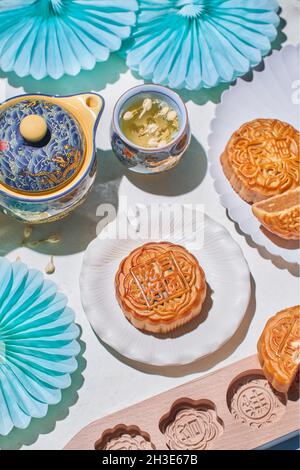 Des gâteaux de lune traditionnels avec garniture servis sur une table avec des moules à pâtisserie près de la bouilloire avec du thé aux herbes dans une pièce lumineuse Banque D'Images