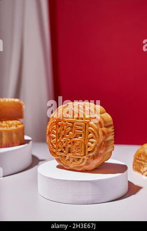 Gâteau de lune traditionnel chinois sucré cuit rond servi sur une table avec des fleurs sur fond rouge dans un studio lumineux moderne Banque D'Images