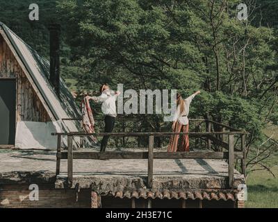 Tout le corps de hippies en boho style danse des vêtements tout en se tenant sur la terrasse près de la cabine en bois pendant le voyage dans la nature Banque D'Images