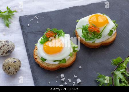 Des canapés appétissants avec du pain croustillant et des œufs de caille frits décorés d'herbes et de caviar servis sur un plateau gris Banque D'Images