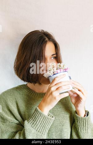 Jeune femme en pull qui sent les fleurs sur fond gris Banque D'Images