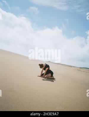 Vue latérale du corps d'une femme pieds nus, se penchant sur les mains tout en s'agenouillant sur une dune de sable dans un désert chaud Banque D'Images