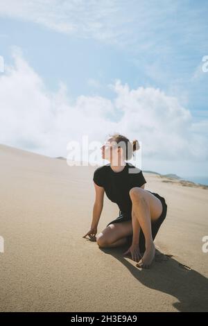 Vue latérale du corps d'une femme pieds nus se penchant sur les mains tout en se squatant sur une dune de sable dans un désert chaud Banque D'Images