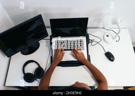 D'en haut, une femme afro-américaine méconnaissable assise à une table et dactylographiant sur un ordinateur portable dans une pièce lumineuse Banque D'Images