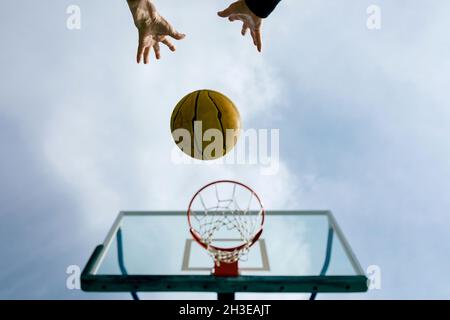 De dessous de crop anonyme personne jetant le ballon de basket-ball dans le cerceau tout en jouant sur le terrain de sport public contre le ciel bleu Banque D'Images