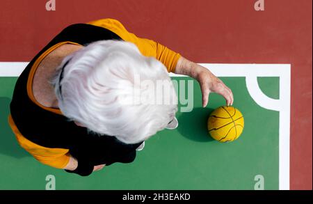 Vue de dessus d'une femelle mature anonyme avec des cheveux gris debout sur le terrain de sport avec du ballon tout en jouant au basket-ball Banque D'Images
