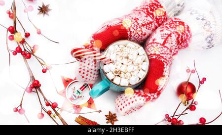 Une tasse de chocolat chaud avec guimauves et canne à sucre en gros plan avec des moufles tricotées entourées de décorations de Noël.Un Noël atmosphérique Banque D'Images