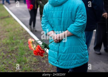 Une femme dans une veste bleue se tient avec des fleurs derrière son dos.Vue de l'arrière.La rue de la ville, la foule des gens.Jour de la victoire.Vie urbaine Banque D'Images