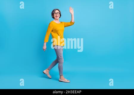 Vue sur toute la longueur du corps de belle gaie joyeuse femme allant bonjour isolée sur fond bleu vif Banque D'Images