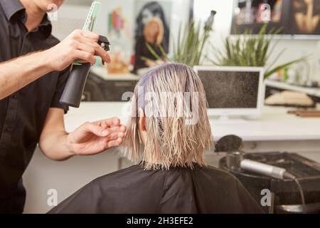 Coiffeur masculin vaporisant de l'eau sur les cheveux du client Banque D'Images