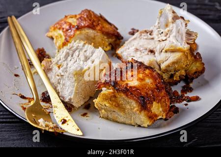 Filet de porc rôti haché en morceaux, servi sur une assiette avec des couverts dorés sur un fond en bois sombre, vue de dessus, gros plan Banque D'Images