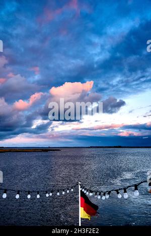 Le drapeau allemand et la fée s'allument à la queue d'un navire sur le Barther Bodden contre le ciel coloré. Banque D'Images