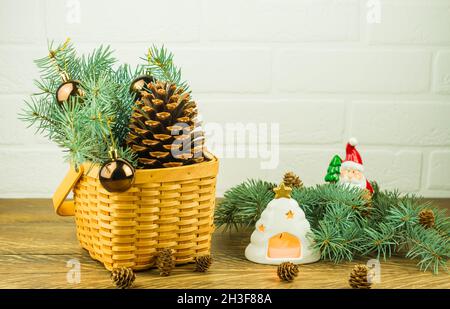 Composition du nouvel an sur une table en bois près d'un panier en osier mural en brique blanche avec branches en épicéa, boules, cône en cèdre. Bougie éclairée dans un chandelier Banque D'Images