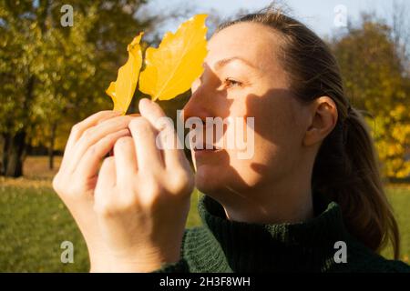 Jeune femme en profil avec des feuilles jaunes, la lumière du soleil, les ombres, les mains gros plan, l'inspiration d'automne. Banque D'Images