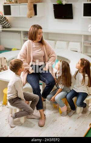 Un professeur de maternelle parle de l'histoire à un groupe d'enfants assis sur une petite chaise à la maternelle Banque D'Images