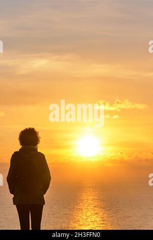 Une femme de randonnée de derrière regardant le lever du soleil sur la mer Banque D'Images