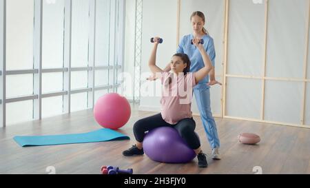 Travailleur médical aidant la femme enceinte à faire des exercices de balle Banque D'Images