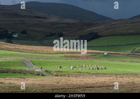 SwInside, alias Sunkenkirk cercle en pierre au soleil brillant; colline de fond dans l'ombre parsemée de moutons blancs, arbres et maison de ferme blanche sous le nuage foncé. Banque D'Images