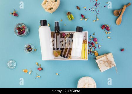 Flacons vides en verre et ambré.Beauté et concept cosmétique sur table bleue avec fleurs autour Banque D'Images