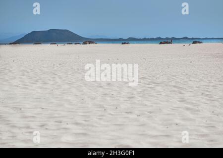 Vue paradisiaque sur la plage de sable blanc avec des abris en pierre et montagne en arrière-plan à Corralejo, Fuerteventura, îles Canaries, Espagne Banque D'Images