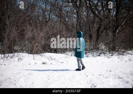 Une femme caucasienne se trouve sur une route enneigée.Une jeune femme en vêtements d'hiver chauds se promède dans la forêt en hiver givré jour ensoleillé, vue latérale Banque D'Images