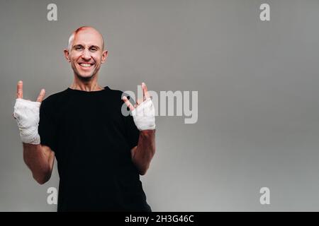 Un homme frappé avec ses mains enveloppé dans un T-shirt noir sur fond gris, qui ressemble à un drogué et un drogué. Banque D'Images