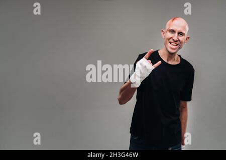 Un homme frappé avec ses mains enveloppé dans un T-shirt noir sur fond gris, qui ressemble à un drogué et un drogué. Banque D'Images