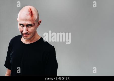 Un homme frappé dans un T-shirt noir sur fond gris, qui ressemble à un drogué et un drogué. Banque D'Images