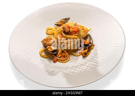 Spaghetti aux fruits de mer, pâtes aux moules, palourdes et sauce tomate à la cerise fraîche dans une assiette blanche isolée sur du blanc Banque D'Images