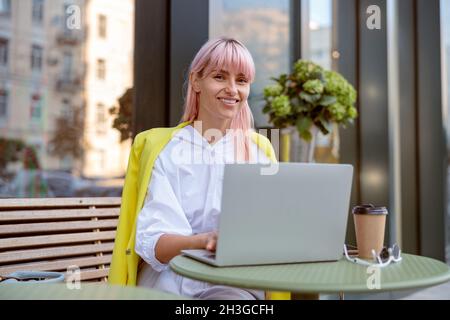 Une jeune femme joyeuse utilisant un ordinateur portable dans un café en plein air Banque D'Images