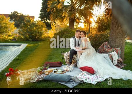 Newlyweds ' dîner sur la pelouse au coucher du soleil.Un couple assis et de boire du thé au coucher du soleil en France. Banque D'Images