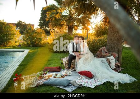 Newlyweds ' dîner sur la pelouse au coucher du soleil.Un couple assis et de boire du thé au coucher du soleil en France. Banque D'Images