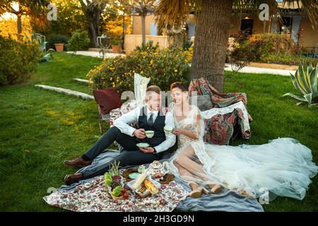 Newlyweds ' dîner sur la pelouse au coucher du soleil.Un couple assis et de boire du thé au coucher du soleil en France. Banque D'Images