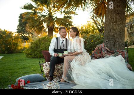 Newlyweds ' dîner sur la pelouse au coucher du soleil.Un couple assis et de boire du thé au coucher du soleil en France. Banque D'Images