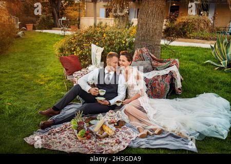 Newlyweds ' dîner sur la pelouse au coucher du soleil.Un couple assis et de boire du thé au coucher du soleil en France. Banque D'Images