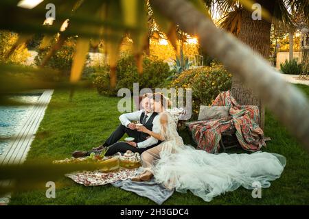 Newlyweds ' dîner sur la pelouse au coucher du soleil.Un couple assis et de boire du thé au coucher du soleil en France. Banque D'Images