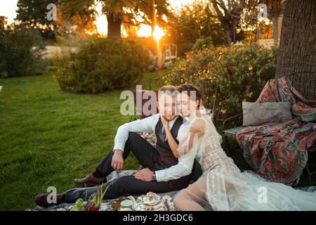 Newlyweds ' dîner sur la pelouse au coucher du soleil.Un couple assis et de boire du thé au coucher du soleil en France. Banque D'Images