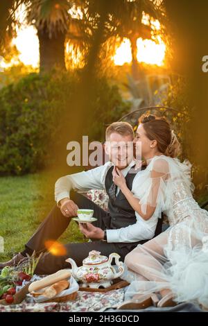 Newlyweds ' dîner sur la pelouse au coucher du soleil.Un couple assis et de boire du thé au coucher du soleil en France. Banque D'Images