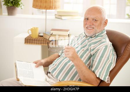 Homme senior lisant dans un fauteuil Banque D'Images