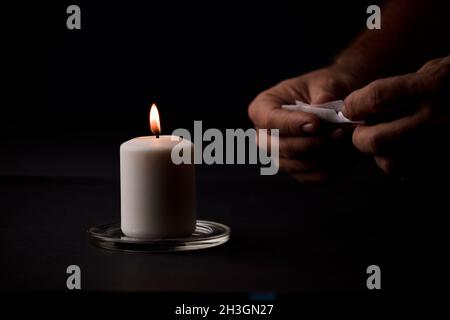 bougie allumée avec une flamme, mains de l'homme tenant un cigare, fond noir.(mise au point sur la bougie). Banque D'Images