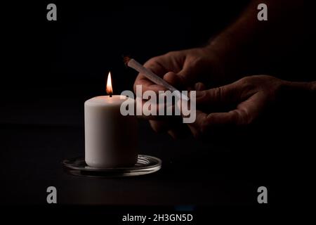 bougie allumée avec une flamme, mains de l'homme tenant un cigare, fond noir.(mise au point sur la bougie). Banque D'Images