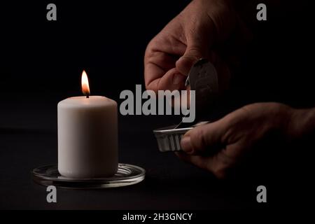 concept de panne d'énergie, bougie éclairée, avec une canelle de conserves dans les mains de l'homme, pauvreté énergétique.(mise au point sur la bougie) Banque D'Images