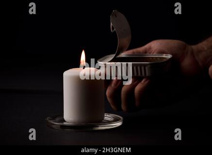 concept de panne d'énergie, bougie éclairée, avec une canelle de conserves dans les mains de l'homme, pauvreté énergétique.(mise au point sur la bougie) Banque D'Images