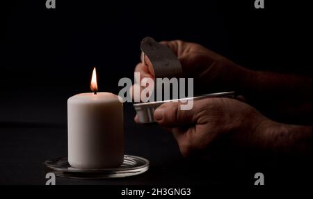 concept de panne d'énergie, bougie éclairée, avec une canelle de conserves dans les mains de l'homme, pauvreté énergétique.(mise au point sur la bougie) Banque D'Images