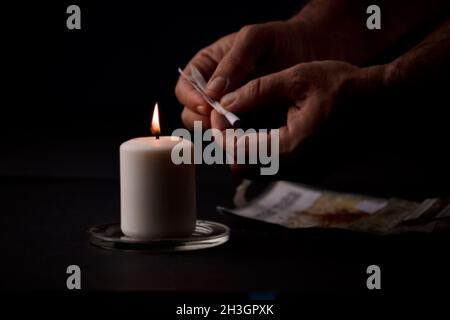 bougie allumée avec une flamme, mains de l'homme tenant un cigare, fond noir.(mise au point sur la bougie). Banque D'Images