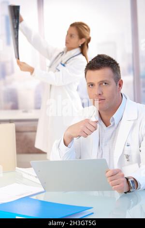 Un médecin de sexe masculin assis à son bureau pour faire de la paperasse Banque D'Images