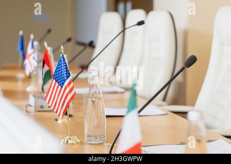 Drapeaux nationaux placés sur une table de conférence en bois avec des microphones, des papiers et des bouteilles d'eau Banque D'Images